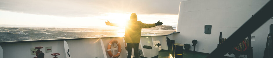 Film-Projekt Antarktis | Sponsoring durch ATLANTIC Hotel Sail City Bremerhaven Person auf Schiffdeck genießt Sonnenuntergang, mit ausgestreckten Armen, Meer im Hintergrund.