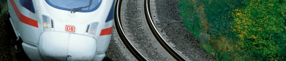 A modern ICE train travels through a green, wooded landscape on a winding route.