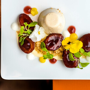 ATLANTIC Hotels Kochbuch Elegant dessert with panna cotta, red fruits, edible flowers and herbs on a white plate.