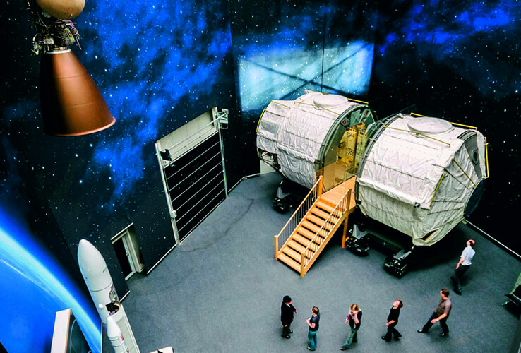 guided tours, space lab Interior view of a space module with stairs, surrounded by space decorations, people looking at the exhibition.