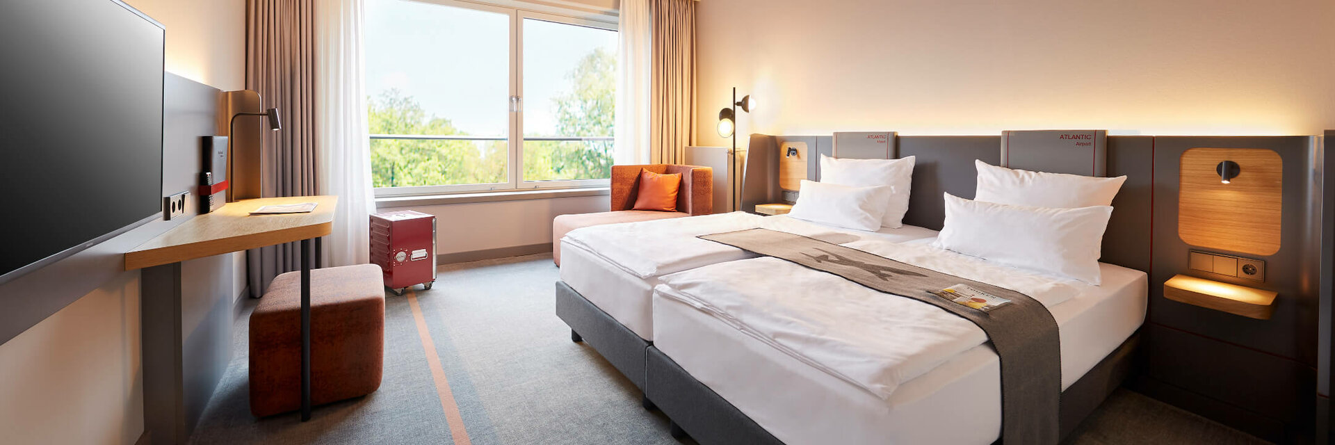 Modern hotel room with two beds, large window, desk and sky motif on the ceiling at the ATLANTIC Hotel Airport.