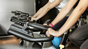 Zwei Personen trainieren auf stationären Fahrrädern im Fitnessraum des Hotels.