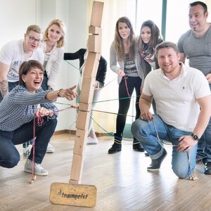 Eine Gruppe von Menschen spielt ein Teamspiel mit Holzklötzen und Seilen in einem Raum.