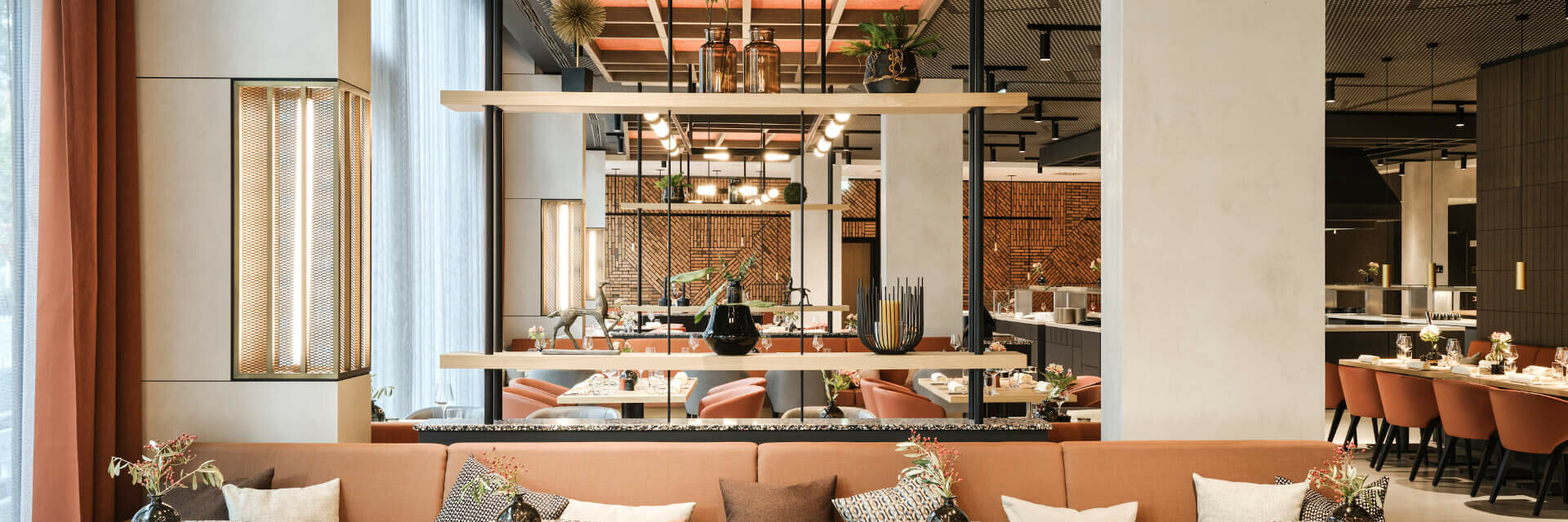 Innenansicht im Restaurant Modernes Restaurant im ATLANTIC Hotel Münster mit stilvollen Tischen, bequemen Sesseln und dekorativen Pflanzen.