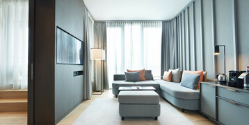 Living area Executive Suite in the ATLANTIC Grand Hotel Bremen Bright hotel room with gray sofa, pillows, carpet, flat-screen TV and coffee machine at the ATLANTIC Grand Hotel Bremen.
