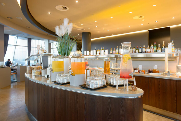 Breakfast buffet in the ATLANTIC Hotel Sail City Drinks station at the ATLANTIC Hotel Sail City with juice dispensers, glasses and a modern interior.