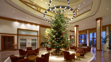 ATLANTIC Hotel Wilhelmshaven | Adventszeit Elegante Hotellobby mit großem, geschmücktem Weihnachtsbaum, umgeben von Sitzgruppen und moderner Beleuchtung.