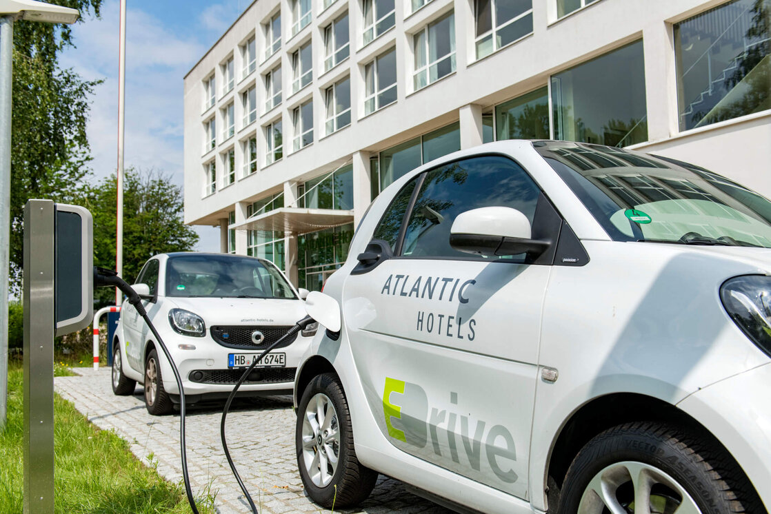 Two electric cars charging at a charging station in front of a modern hotel building.