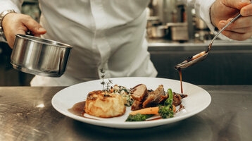 ATLANTIC Hotel Heidelberg Schlossgastronomie Ein Koch richtet Essen in einer professionellen Küche an