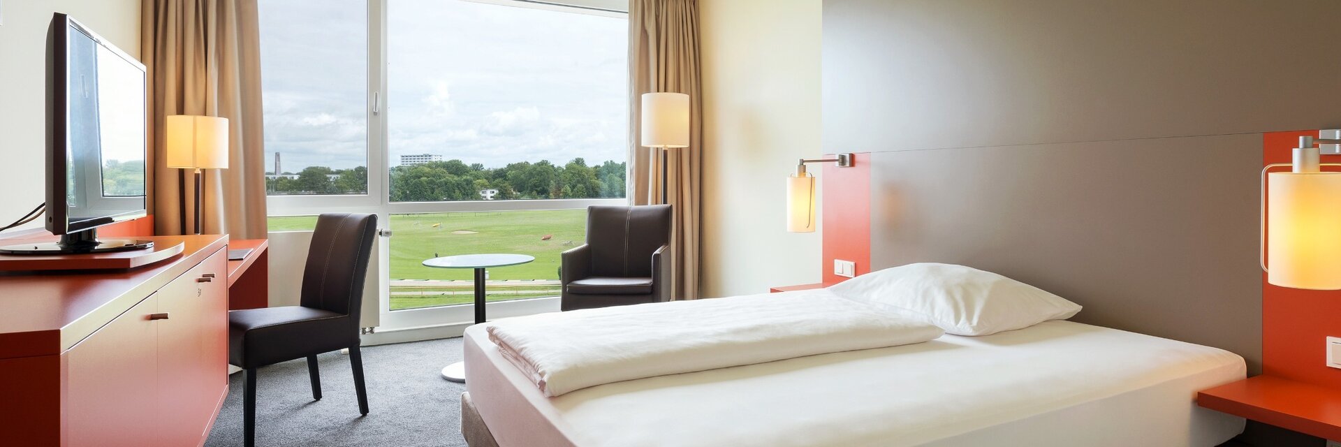 Single room with a view over the race course in the ATLANTIC Hotel Galopprennbahn Bremen Bright hotel room with double bed, desk, armchair and large window with a view of the racecourse.