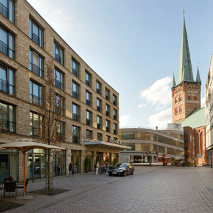 Straßenansicht des ATLANTIC Hotels Lübeck mit Backsteinfassade, daneben eine Kirche mit hohem Turm.
