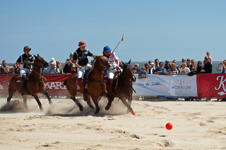 Beach Polo World Cup Sylt Polo match on the beach with riders and horses, spectators in the background, red ball in the foreground.