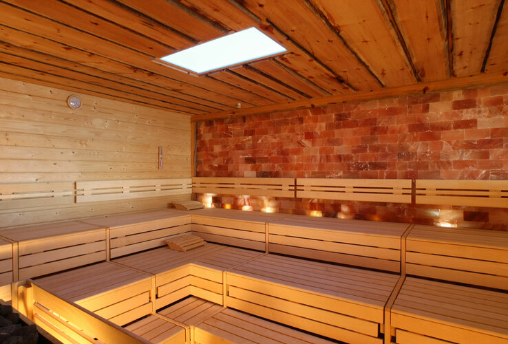 Finnische Sauna im Spa-Bereich des ATLANTIC Hotel Wilhelmhaven Holzverkleidete Sauna mit Sitzbänken und beleuchteter Salzsteinwand für entspannende Wellness-Erlebnisse.