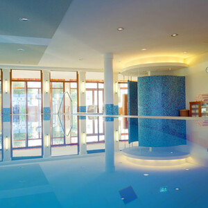 Pool in the ATLANTIC Hotel Wilhelmshaven Bright indoor pool with large windows, blue tiled pillars and sun loungers in the background.