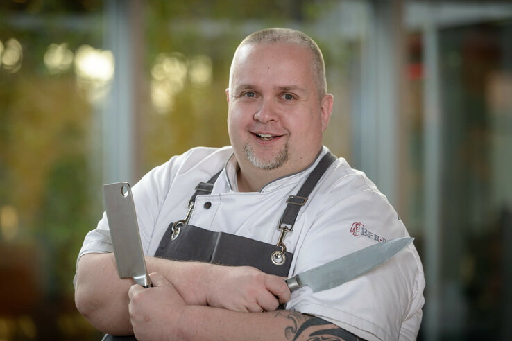 Chef at the CAMPUS restaurant Cook in white uniform with knife and cleaver, smiling in the ATLANTIC Hotel Universum, Bremen.