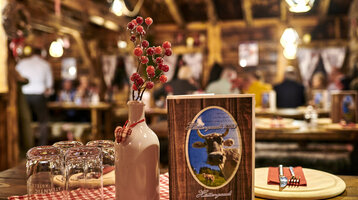 Gemütliche Hotelrestaurant-Szene mit rustikalem Dekor, roter Tischdecke, Vase mit Beeren und Speisekarte im Vordergrund.