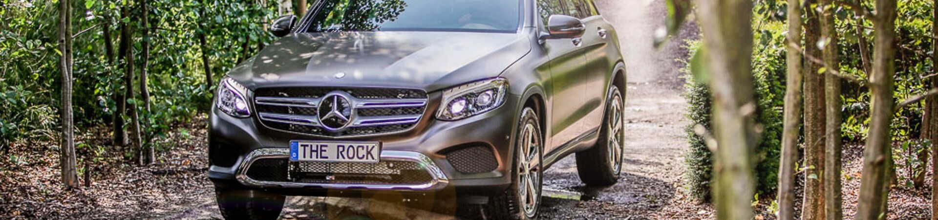 Mercedes Benz all-terrain vehicle at the obstacle course "The Rock" SUV driving on a forest road, surrounded by trees and sunlight.