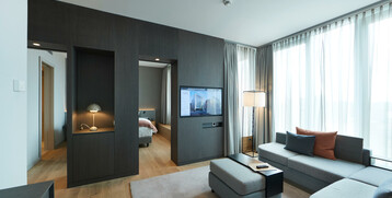Living area of the Executive Suite in the ATLANTIC Grand Hotel Bremen Modern hotel room at the ATLANTIC Grand Hotel Bremen with sofa, flat-screen TV and large windows with curtains.