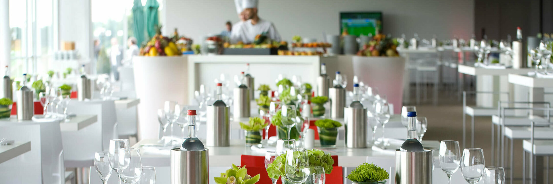 Moderne Events in den ATLANTIC Hotels Helles Hotelrestaurant mit elegant gedeckten Tischen, Blumenarrangements und einem Koch am Buffet im Hintergrund.