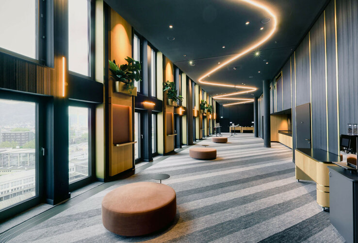 ATLANTIC Hotel Heidelberg Foyer Moderner Hotelflur mit großen Fenstern, geschwungener Beleuchtung, Pflanzen und Sitzgelegenheiten im ATLANTIC Hotel Heidelberg.