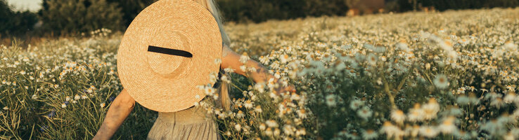 ATLANTIC Hotels Special Rate | Moments Person with straw hat in a flowering field, surrounded by daisies, at sunset.