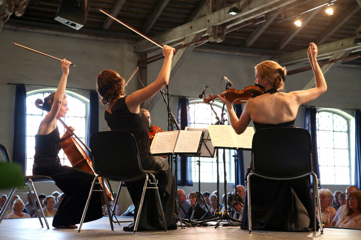 Chamber music at the ATLANTIC Hotel Lübeck String quartet plays in front of an audience in a stylish hall with a wooden beamed ceiling.
