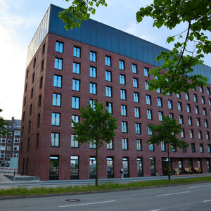 Außenansicht unique by ATLANTIC Hotels Kiel Modernes Backsteinhotel mit vielen Fenstern, umgeben von Bäumen, an einer ruhigen Straße gelegen.