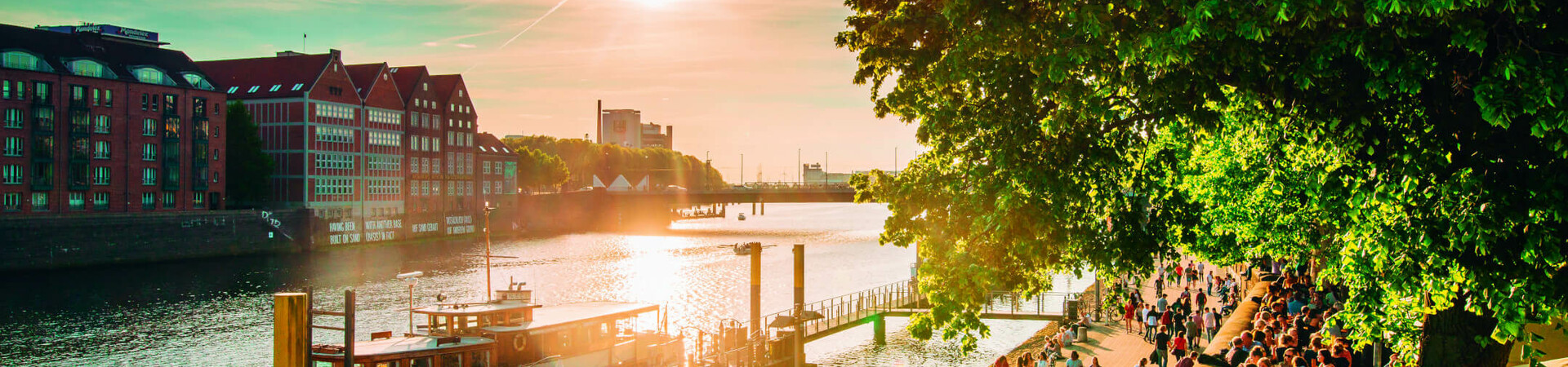 Bremer Schlachte in the spring Sunset on the Weser promenade in Bremen with people, boats and historic buildings in the background.