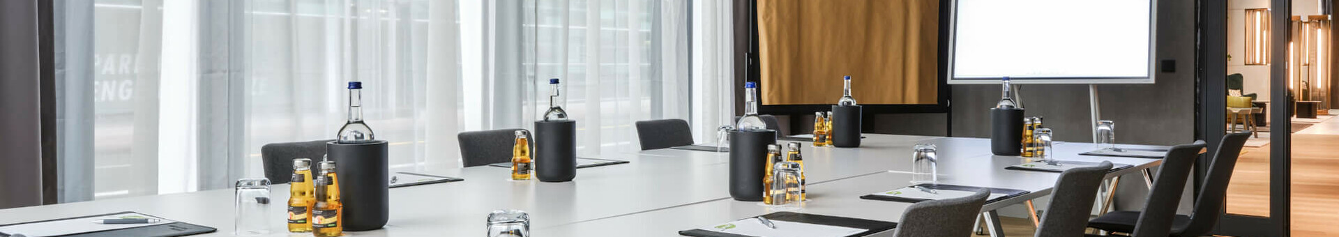 Meeting in ATLANTIC Hotel Münster Modern conference room with large table, chairs, writing materials, water bottles and natural light at the ATLANTIC Hotel Münster.