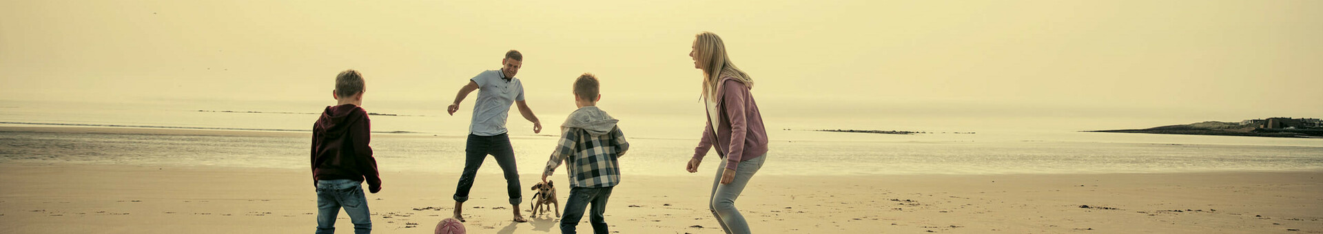 Familienzeit am Strand Familie spielt mit Hund und Ball am sonnigen Strand, Meer im Hintergrund.