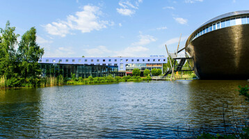 ATLANTIC Hotel Universum in Bremen ATLANTIC Hotel Universum in Bremen next to a lake, modern building, blue sky, green shore vegetation.