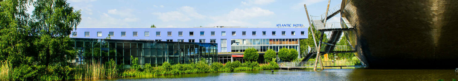 ATLANTIC Hotel Universum in Bremen ATLANTIC Hotel Universum in Bremen next to a lake, modern building, blue sky, green shore vegetation.