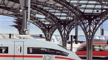 Veranstaltungsticket der Deutschen Bahn für Veranstaltungen in den ATLANTIC Hotels Moderner Bahnhof mit ICE-Zug im Vordergrund und einem weiteren Zug im Hintergrund unter einem gewölbten Glasdach.