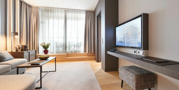 Balcony Suite living area at the Atlantic Grand Hotel Bremen Modern hotel room with sofa, coffee table, TV, large windows and bright furnishings at the ATLANTIC Grand Hotel Bremen.