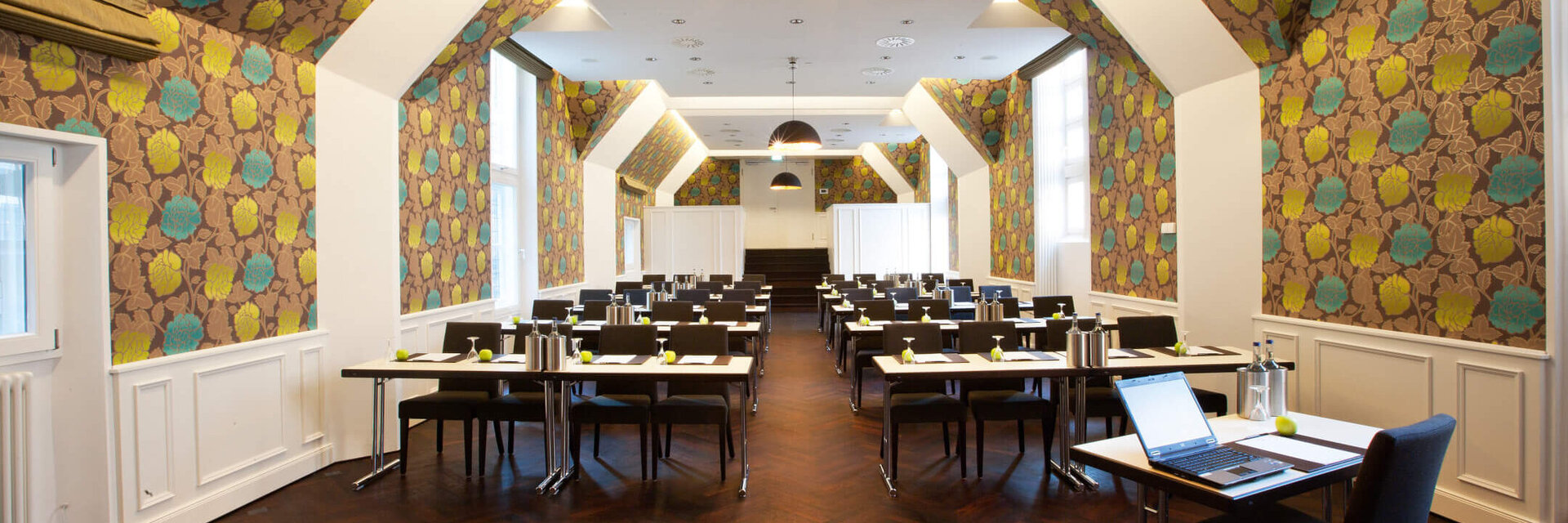 Paralamentarsich bestuhlter Scotland Saal im ATLANTIC Grand Hotel Bremen Moderner Konferenzraum im ATLANTIC Grand Hotel Bremen mit stilvoller Tapete und Tischen in Reihen.