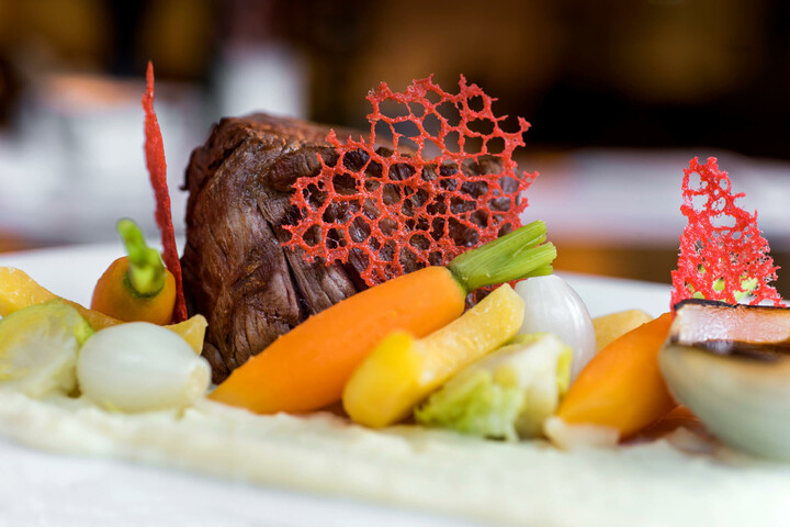Food for meetings and events | ATLANTIC Hotel Lübeck Gourmet dish with tender meat, colorful vegetables and red decoration on a white plate at the ATLANTIC Hotel Lübeck.