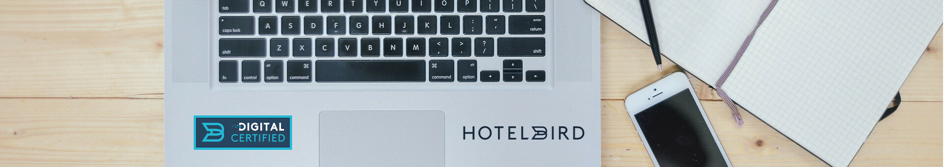 Online Check-In and Check-Out l ATLANTIC Hotels Laptop with "Hotelbird" logo, next to it a smartphone and a notebook on a wooden table.