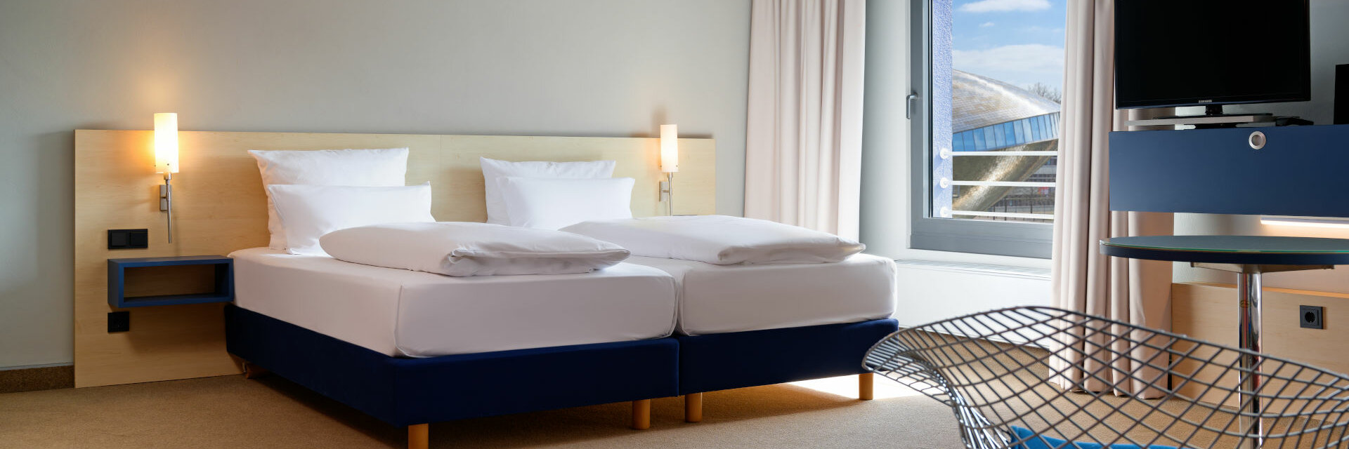 Helles Hotelzimmer mit Doppelbett, modernem Dekor, großem Fenster und TV im ATLANTIC Hotel Universum, Bremen.