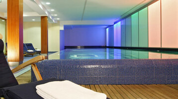 Sunbeds next to a swimming pool in the ATLANTIC Grand Hotel Travemünde Indoor pool at the ATLANTIC Grand Hotel Travemünde with sun loungers, colorful lighting and a relaxing atmosphere.