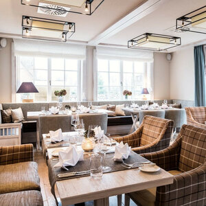 Elegantes Hotelrestaurant mit gedeckten Tischen, stilvollen Sitzmöbeln und großen Fenstern, die natürliches Licht hereinlassen.