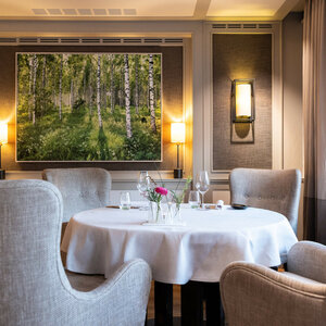 Fotokunst von Fotograf Andreas Wagner im Restaurant Tipken's by Nils Henkel | Severin*s Resort & Spa Sylt Elegantes Restaurant mit gedecktem Tisch, bequemen Sesseln und einem Gemälde von Birkenwald an der Wand.