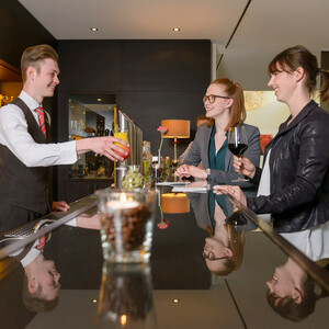ATLANTIC Hotel Lübeck – Bar Bartender serves cocktails to two women at the stylish hotel bar of the ATLANTIC Hotel Lübeck.