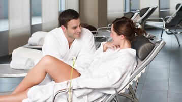 Ein Paar in weißen Bademänteln entspannt auf Liegen im Spa-Bereich eines Hotels.