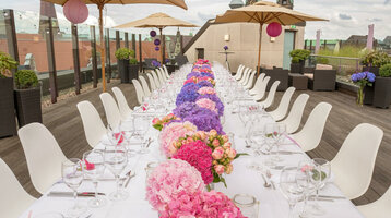 Hochzeitstafel auf der Dachterrase des ATLANTIC Grand Hotel Bremen Lange Tafel mit weißen Stühlen und bunten Blumenarrangements auf einer Dachterrasse des ATLANTIC Grand Hotel Bremen.