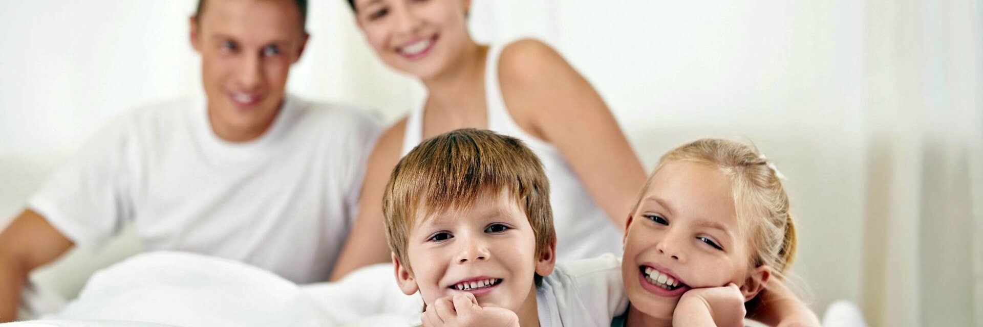 Familie im ATLANTIC Hotel Lübeck Familie entspannt lächelnd auf einem Bett im ATLANTIC Hotel Lübeck, helle und freundliche Atmosphäre.