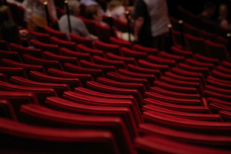GOP theater Essen Rows of empty, red theater seats in an auditorium with blurred people in the background.