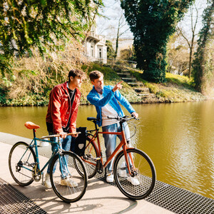 Bike paths in Bremen l Bike it surrounding area ©WFB - Jonas Ginter Two people with bicycles are standing on the shore of a lake, surrounded by green nature and trees.