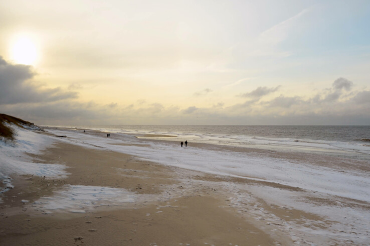 winter walk in Sylt Snow-covered beach at sunset, gentle waves, a few walkers in the distance.