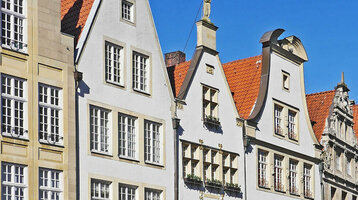 Guided tour of the old town of Münster with ATLANTIC Hotel Münster Historic row of houses with arcades and red roofs on Prinzipalmarkt in Münster under a blue sky.