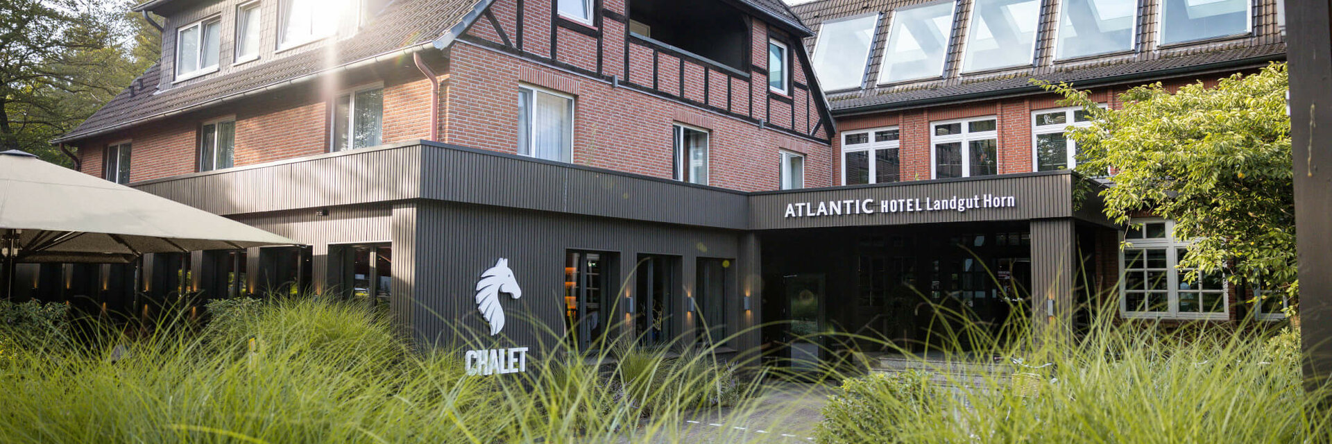Half-timbered house of the ATLANTIC Hotel Landgut Horn Bremen with green garden in the foreground and sunshine on the roof.